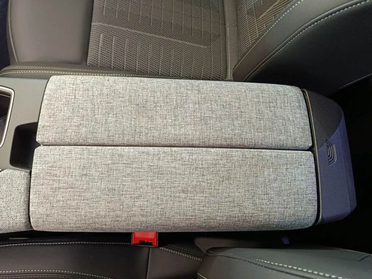 Gros plan sur l'accoudoir central gris clair en tissu et cuir, avec couture blanche, intérieur Peugeot 3008 2025.
