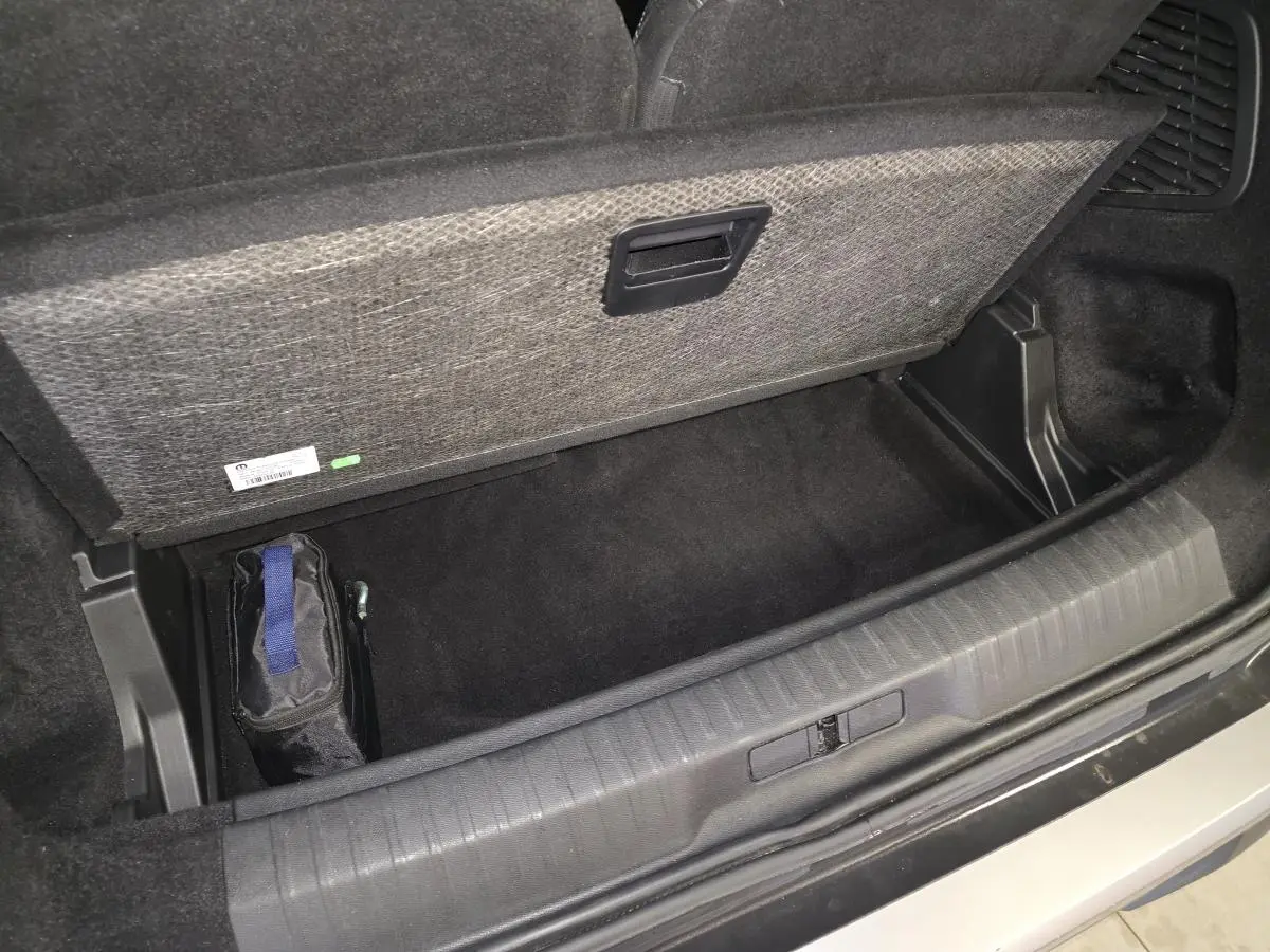 Coffre ouvert en vue plongeante d’un Peugeot 5008 gris, montrant le rangement sous plancher avec trousse noire.