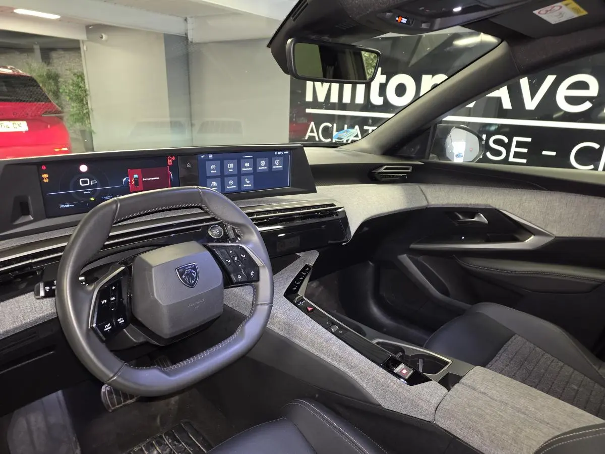 Vue intérieure côté conducteur du Peugeot 5008 gris 2025, avec tableau de bord numérique panoramique et volant compact cuir.
