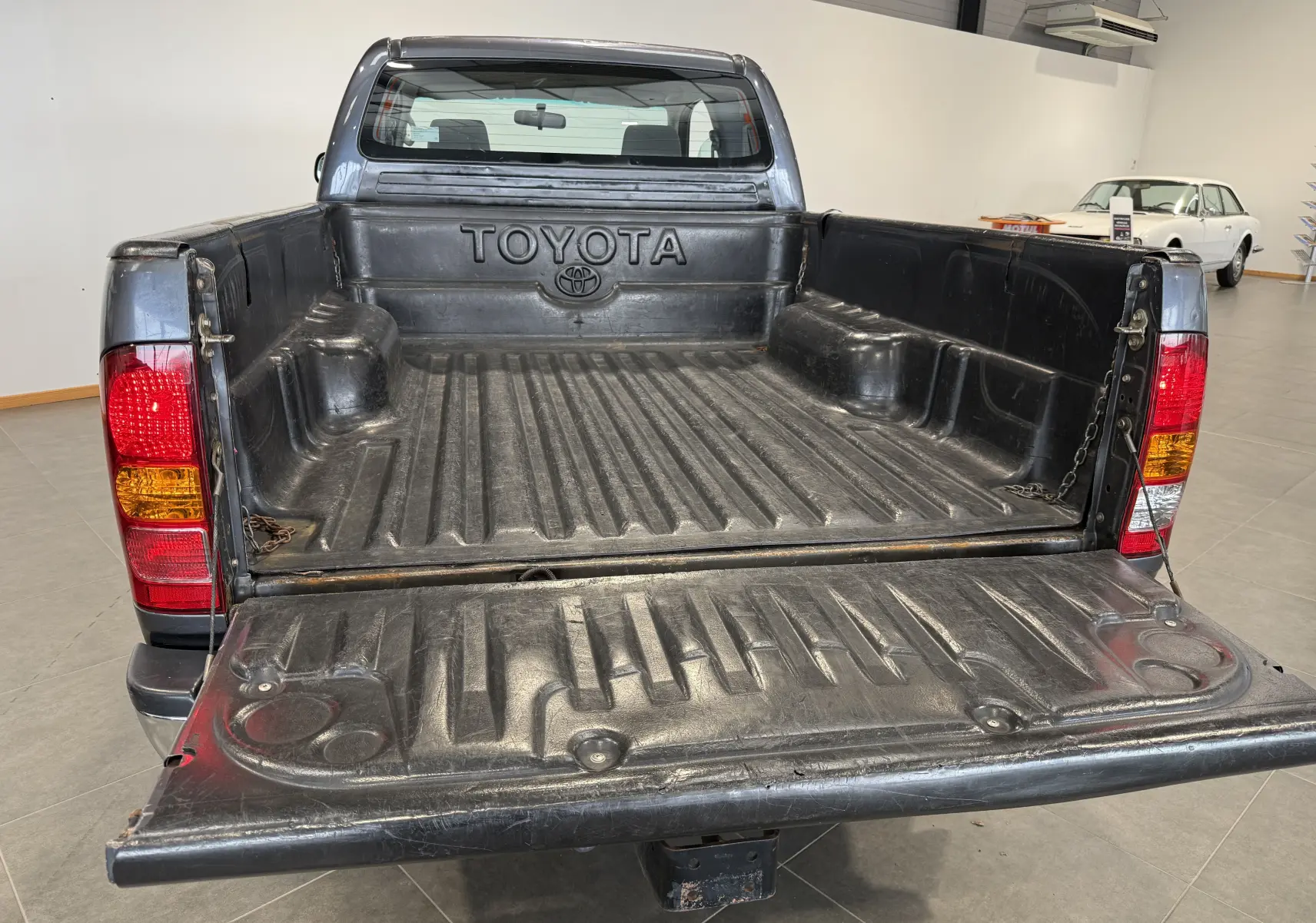 Vue arrière ouverte du Toyota Hilux X-Tra Cabine gris 2009, mettant en valeur la benne et les feux arrière rouges et orange.