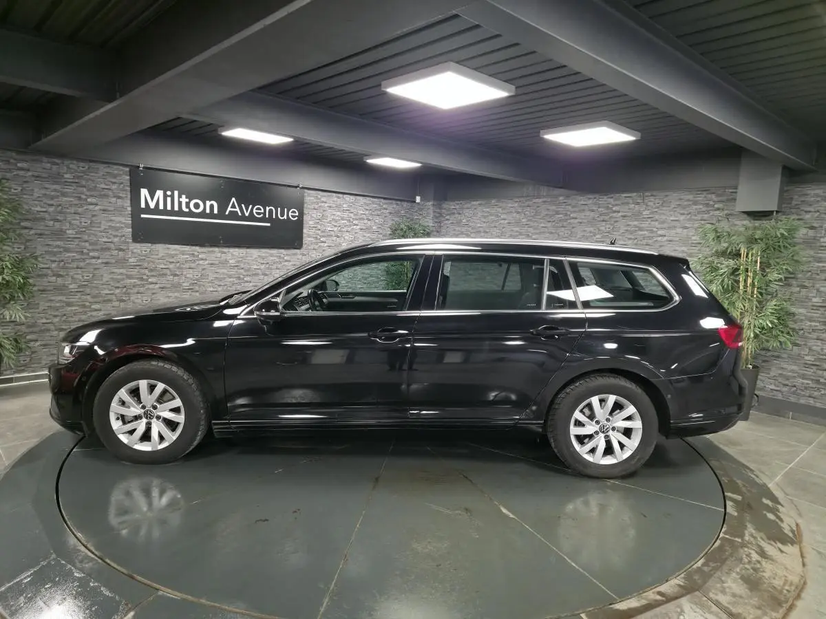 Volkswagen Passat SW noire vue de profil côté gauche dans un showroom avec éclairage intérieur.