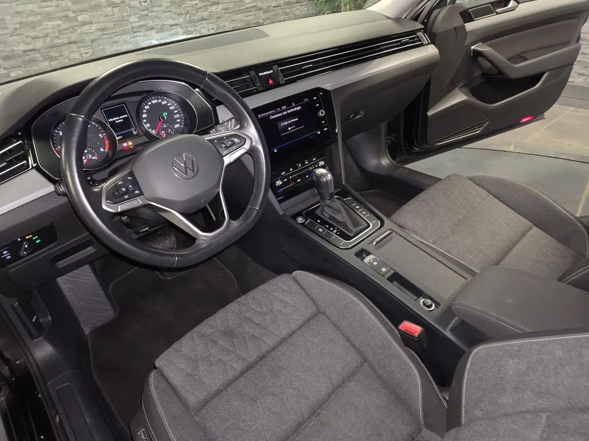 Vue intérieure côté conducteur de la Volkswagen Passat SW 2024, volant cuir noir et sièges tissu gris.