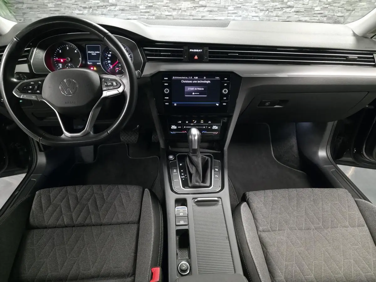 Vue intérieure avant de la Volkswagen Passat SW 2024, tableau de bord noir avec volant multifonction et console centrale moderne.