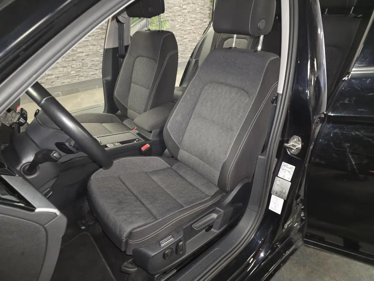 Vue intérieure côté conducteur de la Volkswagen Passat SW 2024 noire, sièges tissu gris avec surpiqûres blanches.