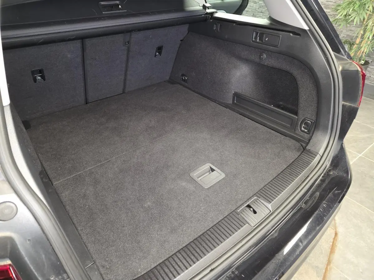 Coffre ouvert d'une Volkswagen Passat SW noire, montrant l'espace de chargement et les finitions intérieures en tissu gris.