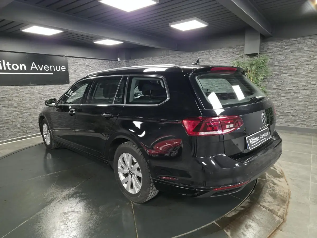 Volkswagen Passat SW noire vue 3/4 arrière droit dans un showroom avec mur en pierre grise.
