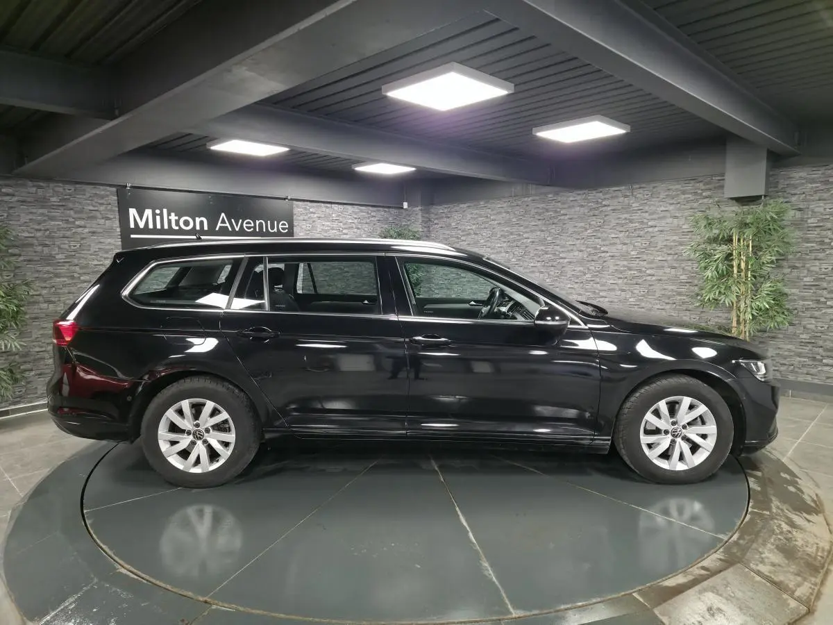 Volkswagen Passat SW noir vue de profil côté gauche dans un showroom avec sol gris et mur en pierre.