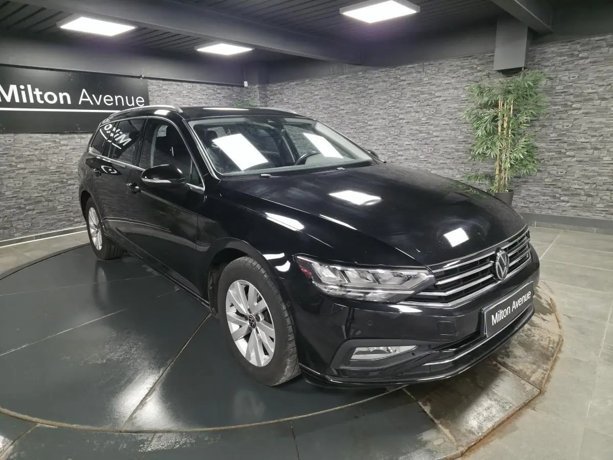 Volkswagen Passat SW noire vue 3/4 avant droit en intérieur avec calandre chromée et jantes alliage 16 pouces.
