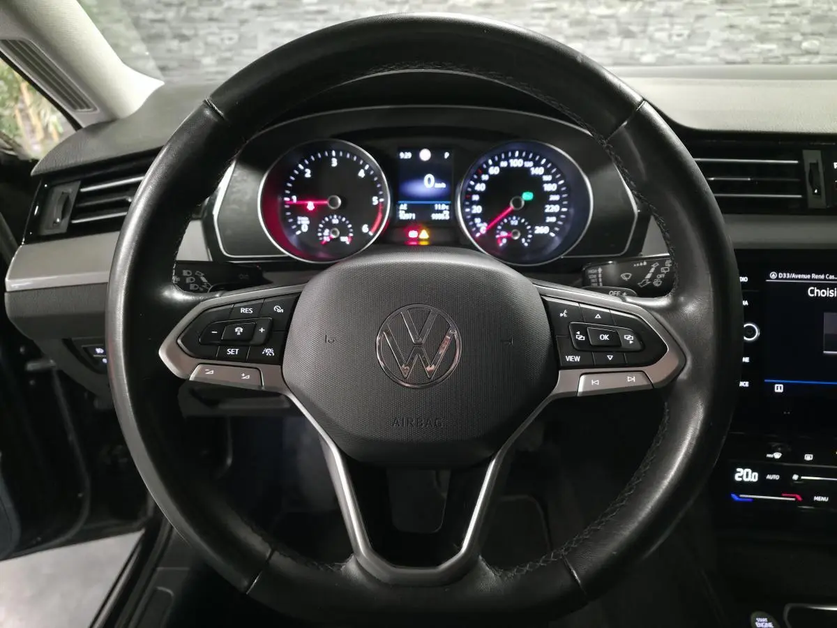 Vue rapprochée du volant cuir noir multifonction d'une Volkswagen Passat 2024 avec tableau de bord et écran tactile visibles.