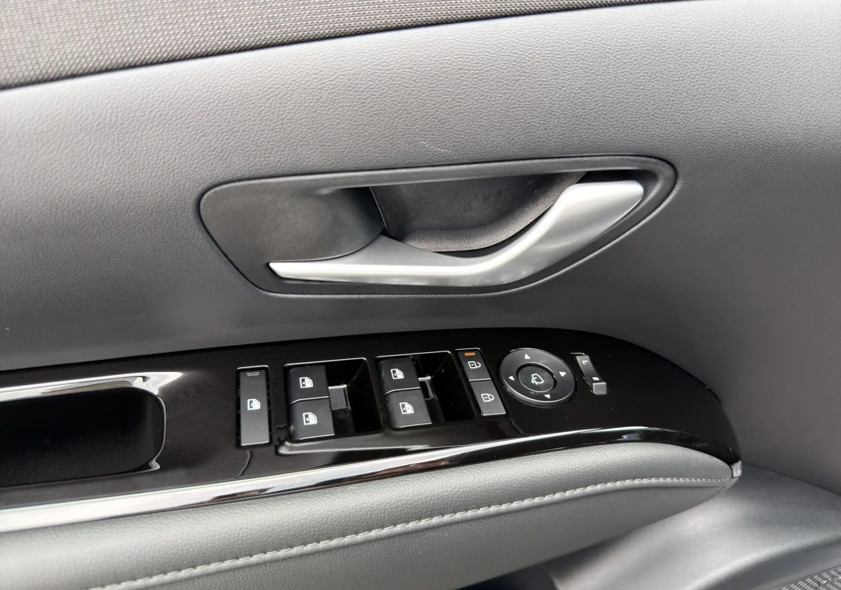 Poignée de porte intérieure côté conducteur avec commandes électriques des vitres et rétroviseurs sur Hyundai Tucson gris foncé 2026.