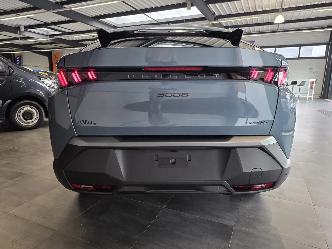 Vue arrière d'un Peugeot 3008 hybride bleu avec feux LED 3 griffes et bandeau noir laqué entre les feux.
