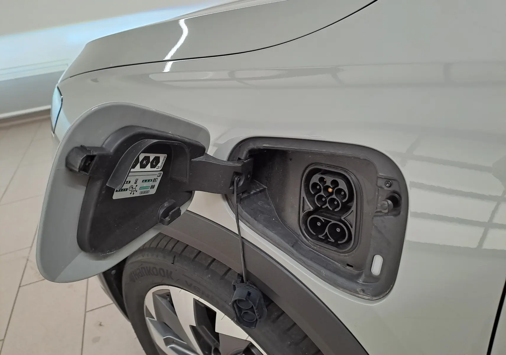 Prise de recharge ouverte côté gauche sur Skoda Kodiaq gris perle avec jante alliage 19 pouces visible.