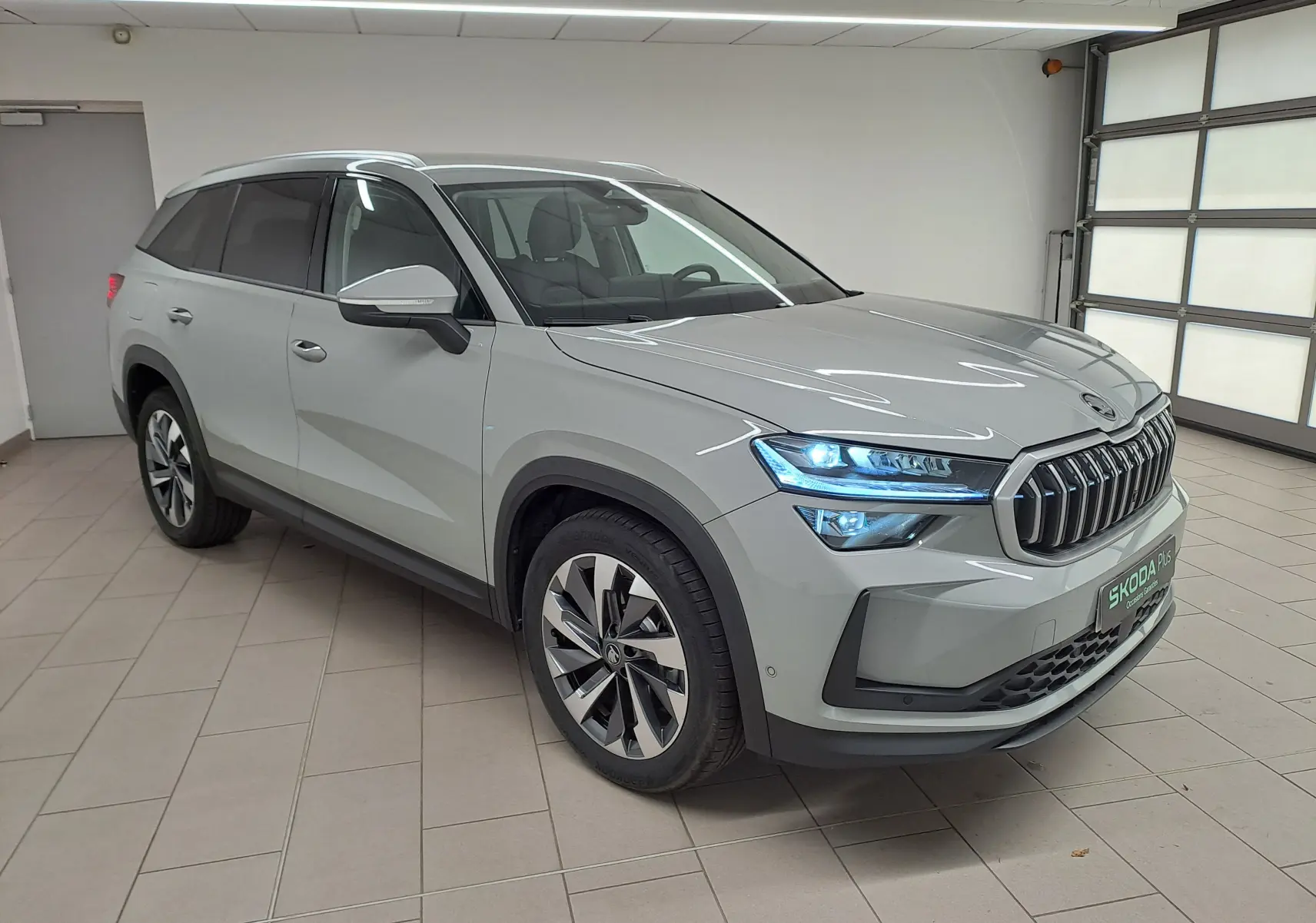 Vue 3/4 avant du Skoda Kodiaq gris perle 2025 avec phares LED allumés et jantes alliage 19 pouces anthracite.