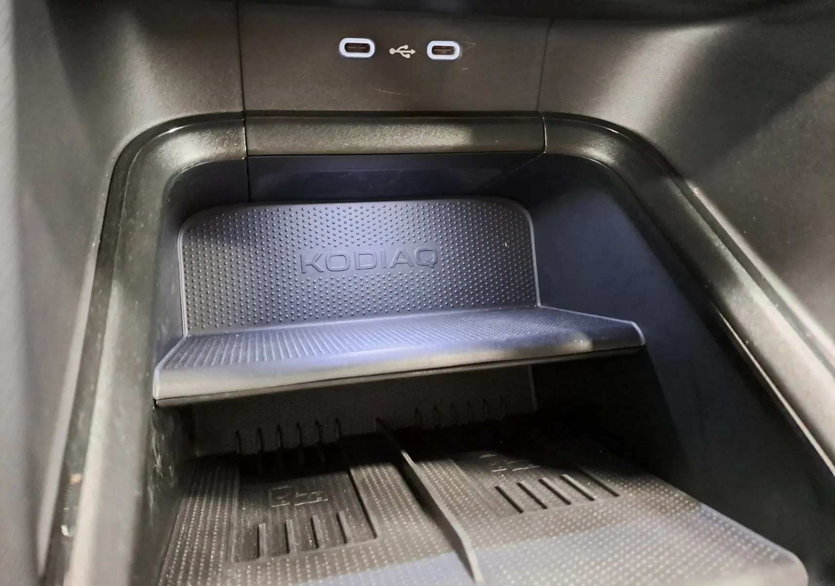 Gros plan sur la zone de recharge sans fil avec logo KODIAQ et deux ports USB-C dans un Skoda Kodiaq gris perle.