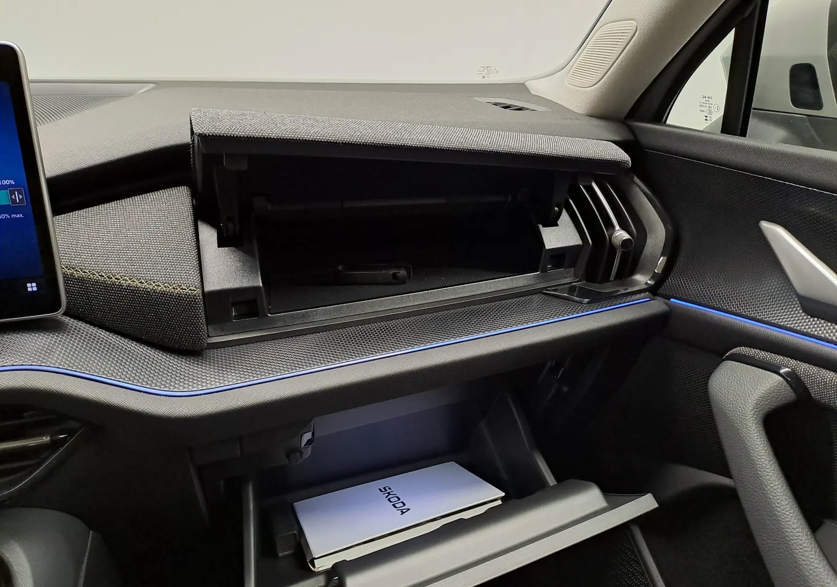 Intérieur du Skoda Kodiaq 2025 gris perle, vue du tableau de bord côté passager avec boîtes à gants ouvertes et éclairage d’ambiance bleu.