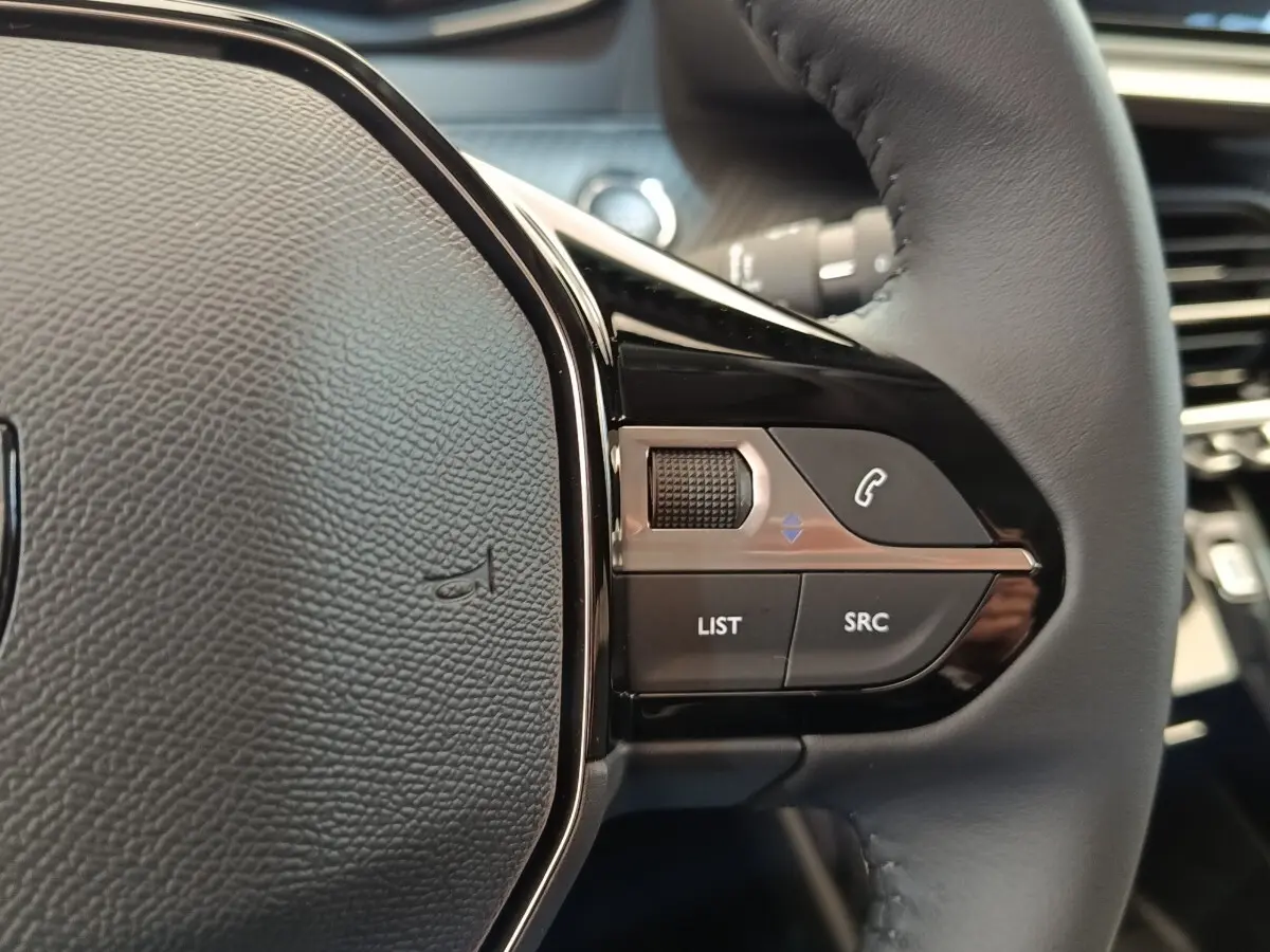 Gros plan sur la partie droite du volant cuir noir du Peugeot 208 électrique 2024 avec commandes audio intégrées.