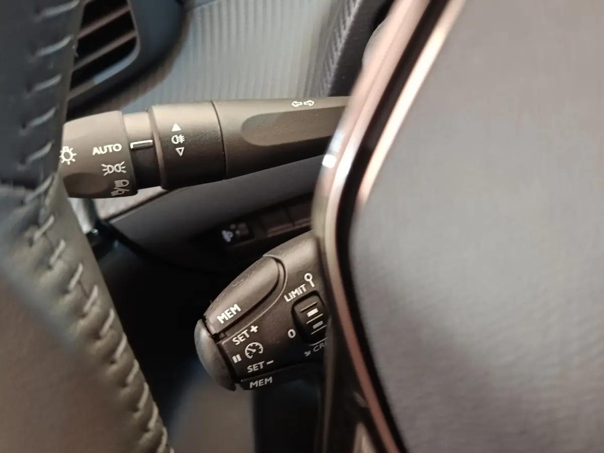 Gros plan sur les commandes au volant cuir noir de la Peugeot 208 électrique blanche, avec régulateur de vitesse.