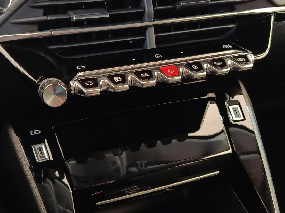 Vue rapprochée de la console centrale noire brillante avec boutons chrome et touches de commande sur Peugeot 208 électrique blanche.