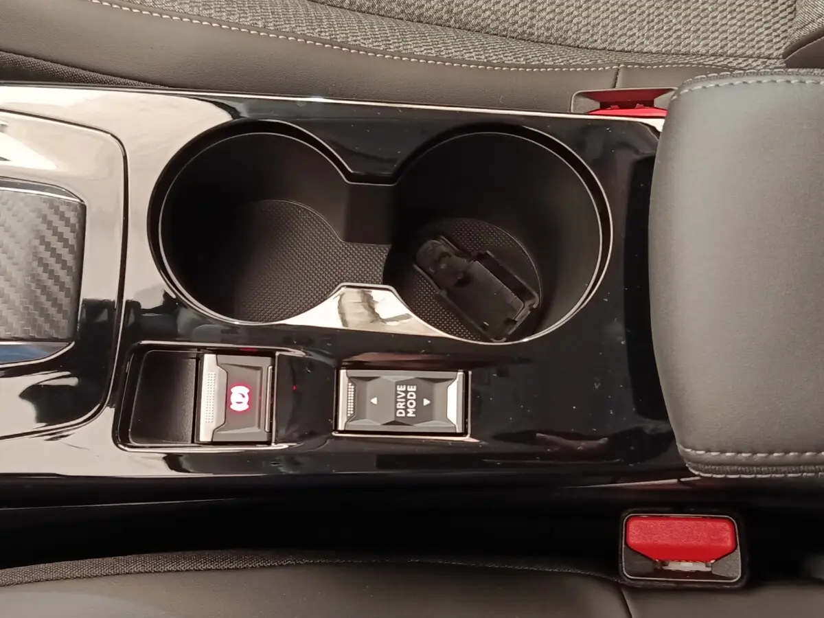 Gros plan sur la console centrale noire brillante de la Peugeot 208 électrique 2024, avec commandes frein à main et mode de conduite.