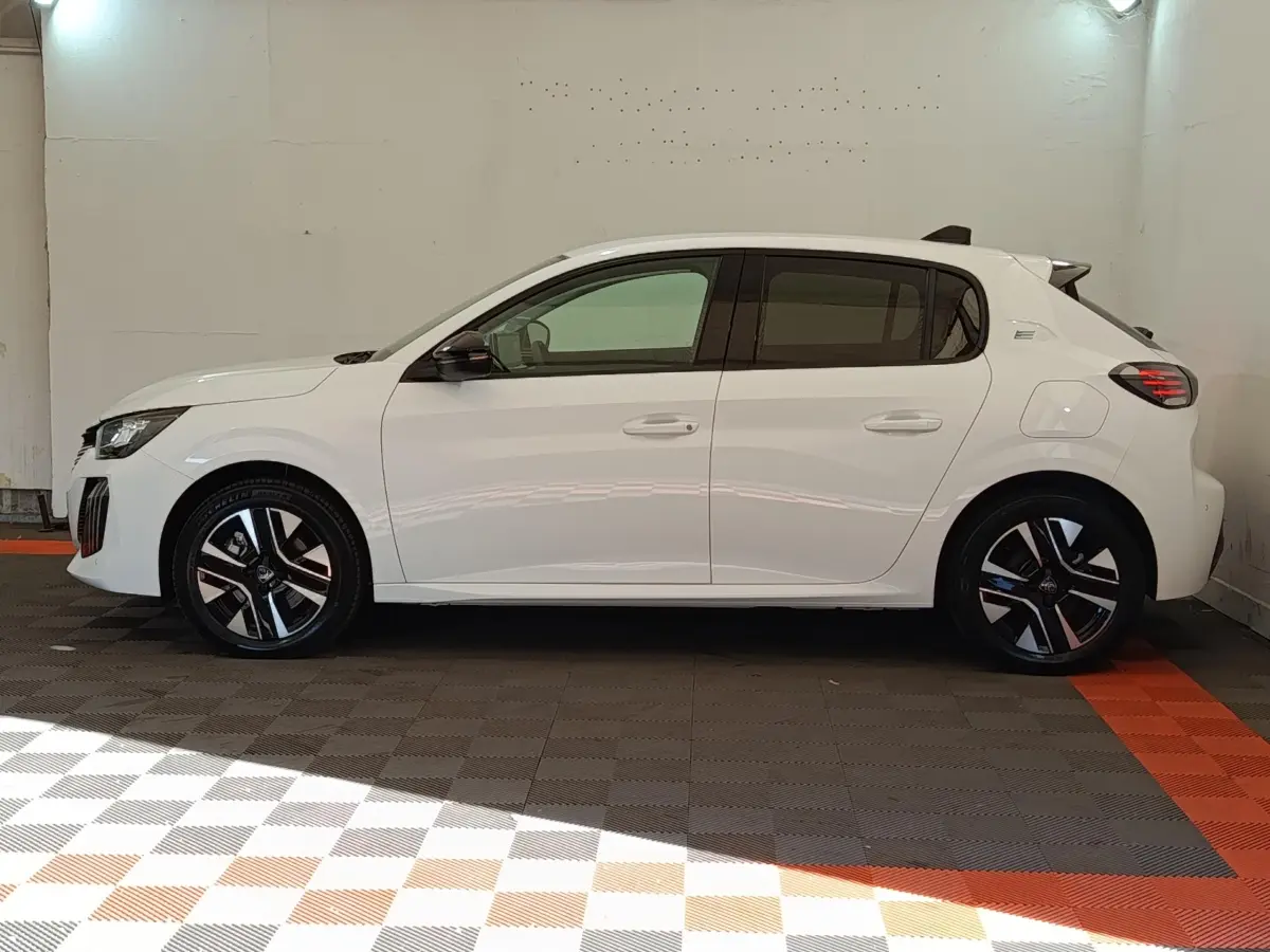 Peugeot 208 électrique blanche vue de profil côté gauche, avec jantes noires et détails bleus sur les roues.