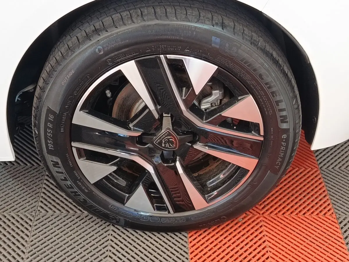 Gros plan sur la roue avant droite de la Peugeot 208 électrique blanche, jante alliage noir et argentée design moderne.