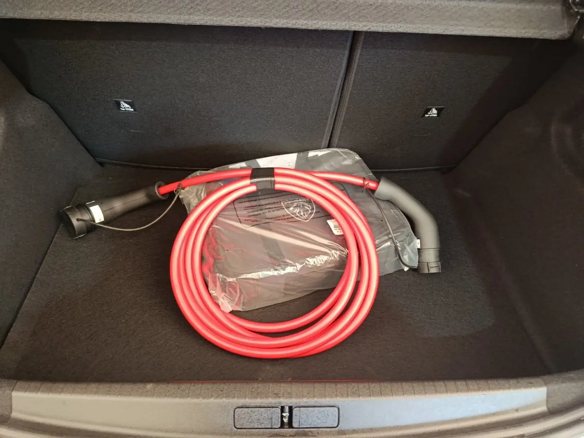 Coffre ouvert d’une Peugeot 208 électrique 2024 avec câble de charge rouge enroulé et sac de rangement noir.