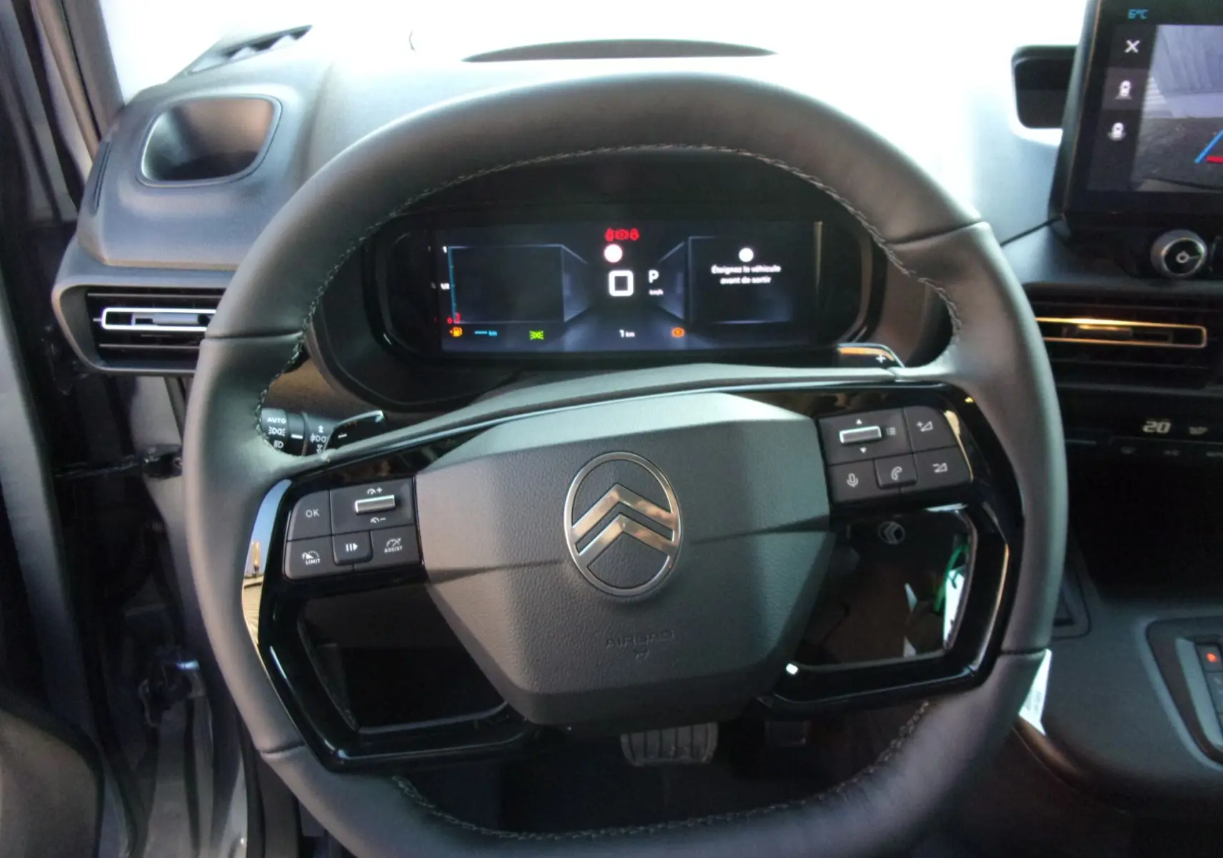 Vue intérieure centrée sur le volant noir du Citroën Berlingo 2025 avec tableau de bord numérique et commandes intégrées.