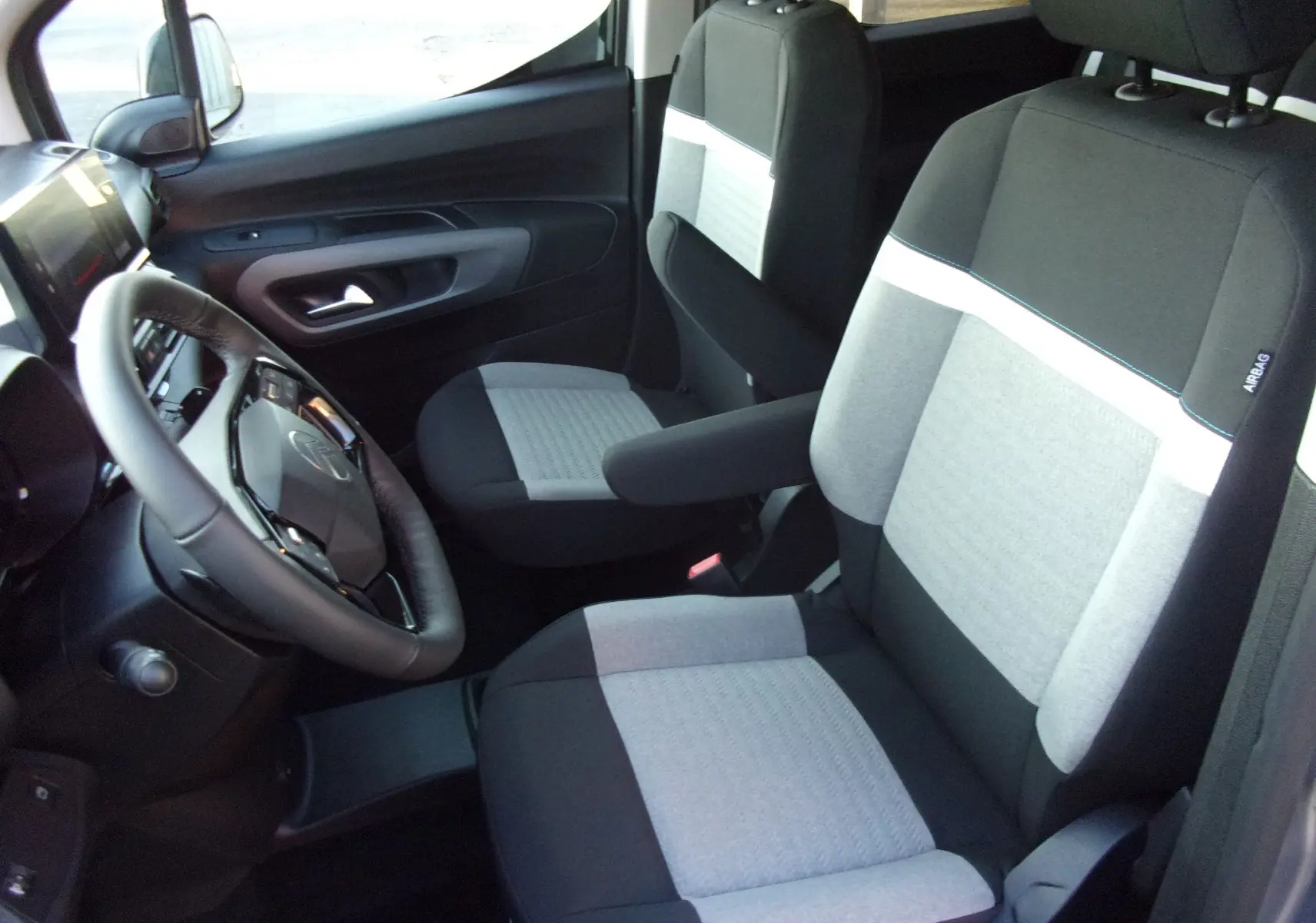 Vue intérieure côté conducteur du Citroën Berlingo 2025 gris Artense, sièges bicolores avec accoudoirs et volant multifonction.