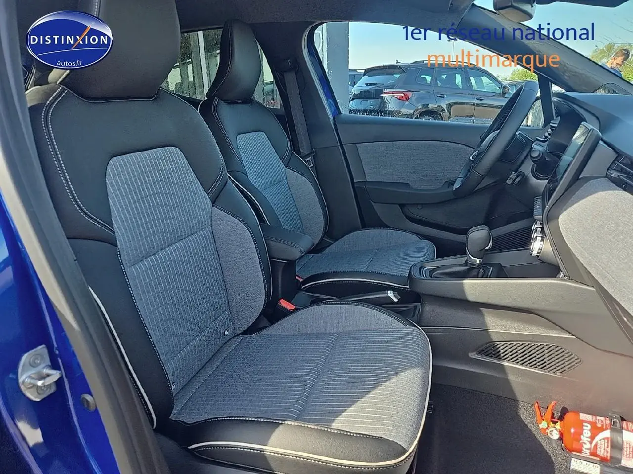 Intérieur avant de la Renault Clio V bleu iron, sièges sport gris et noir avec accoudoir central et tableau de bord visible.