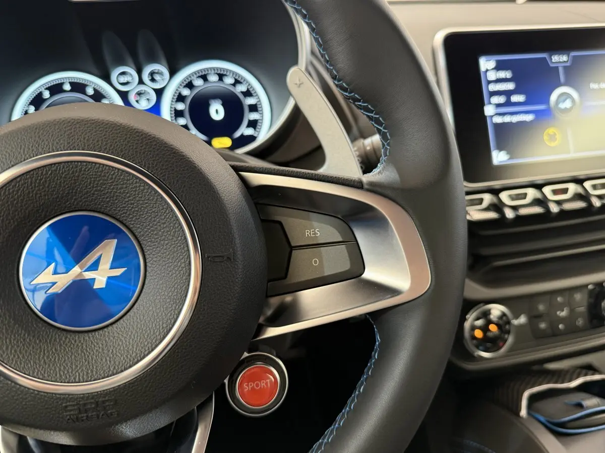 Gros plan sur le volant cuir de l'Alpine A110 Légende 2019 avec bouton rouge Sport et tableau de bord numérique.