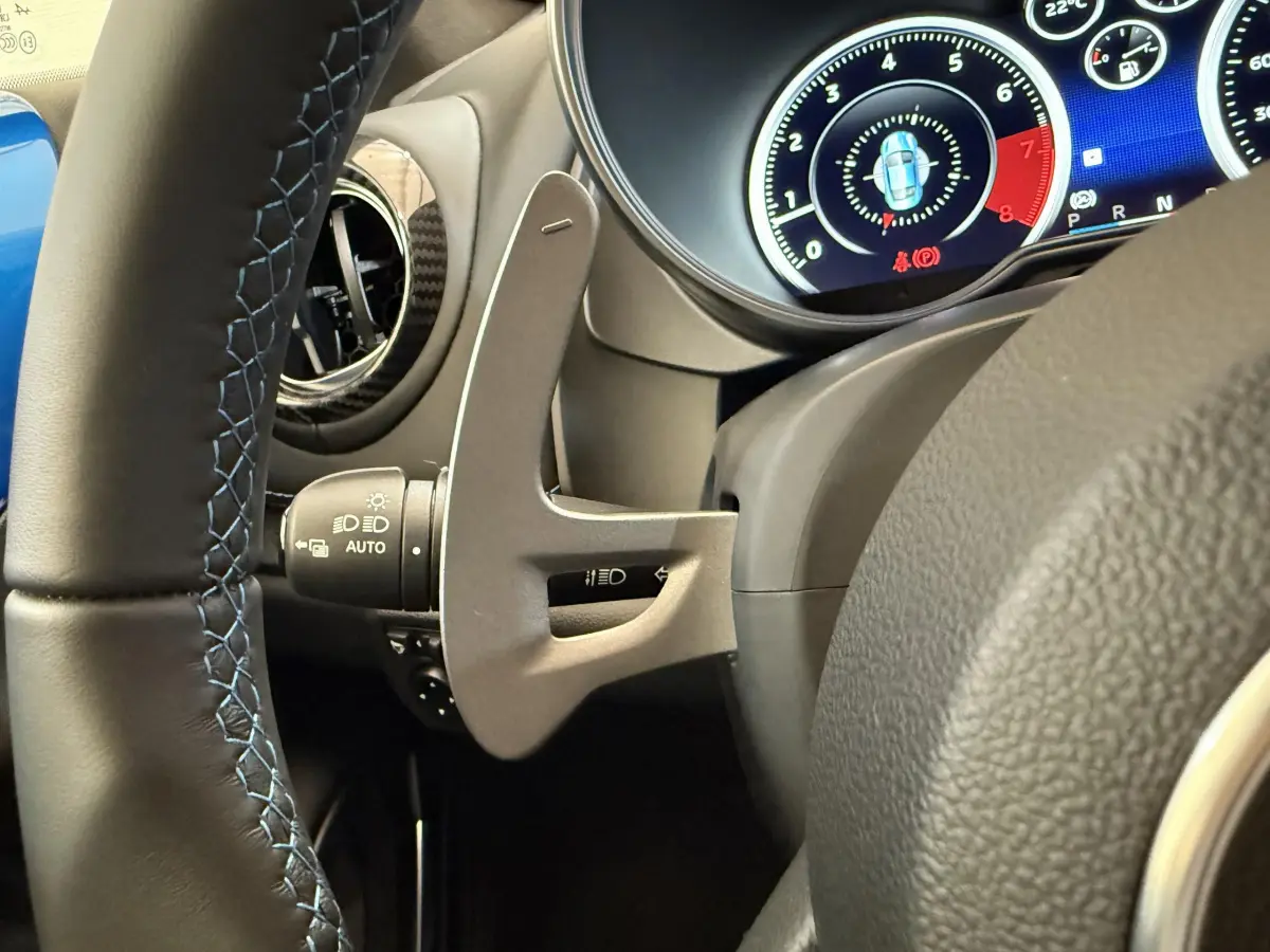 Gros plan sur le volant cuir noir avec surpiqûres bleues et les commandes du tableau de bord numérique de l'Alpine A110 Legende 2019.