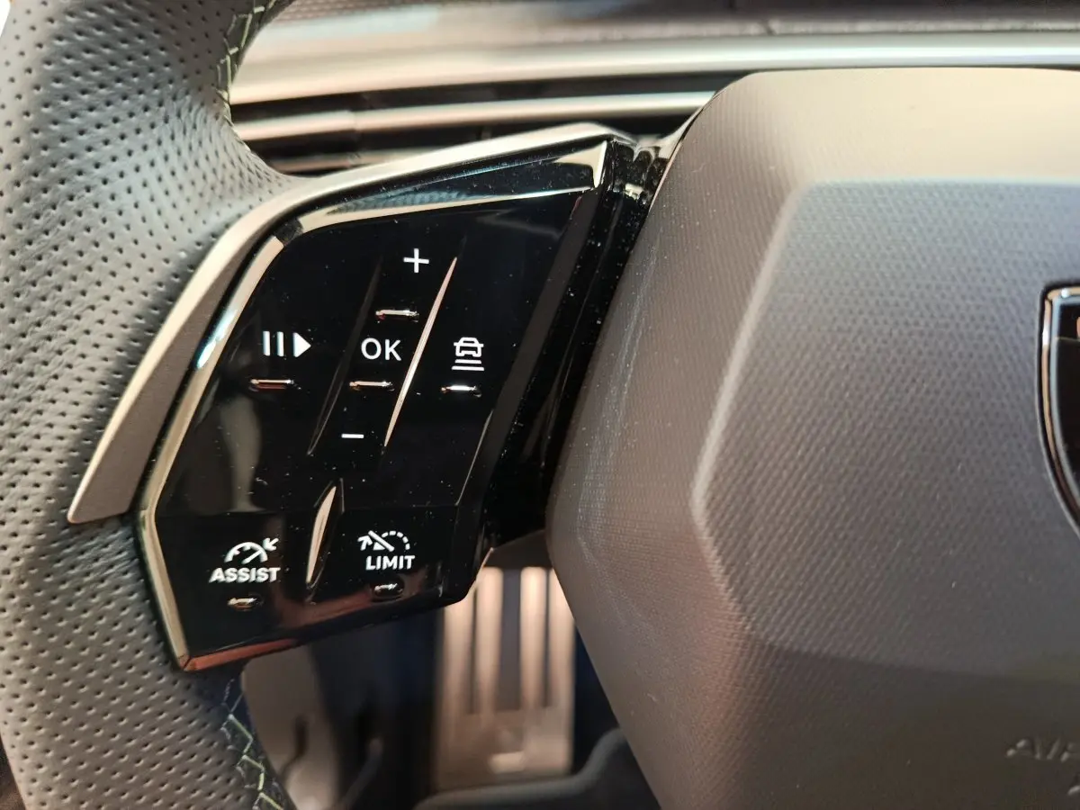 Gros plan sur les commandes multifonctions noires du volant cuir perforé du Peugeot 3008 blanc hybride 2025.