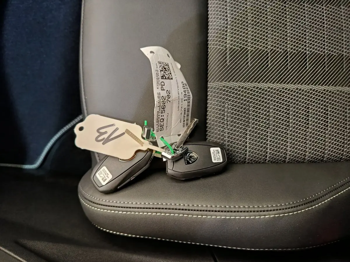Gros plan sur deux clés Peugeot posées sur un siège avant en tissu gris à motifs et cuir noir.