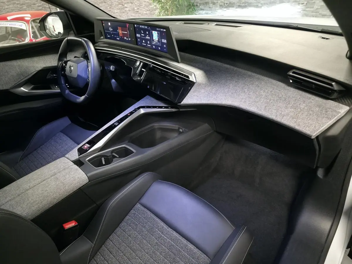 Intérieur avant droit du Peugeot 5008 blanc 2025, tableau de bord tissu gris, double écran HD panoramique et volant compact noir.