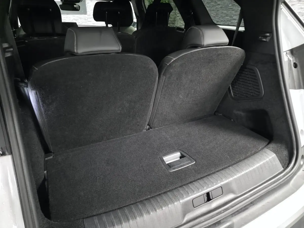 Coffre ouvert vu de l'arrière d'un Peugeot 5008 blanc, montrant la banquette rabattue et l'intérieur noir.