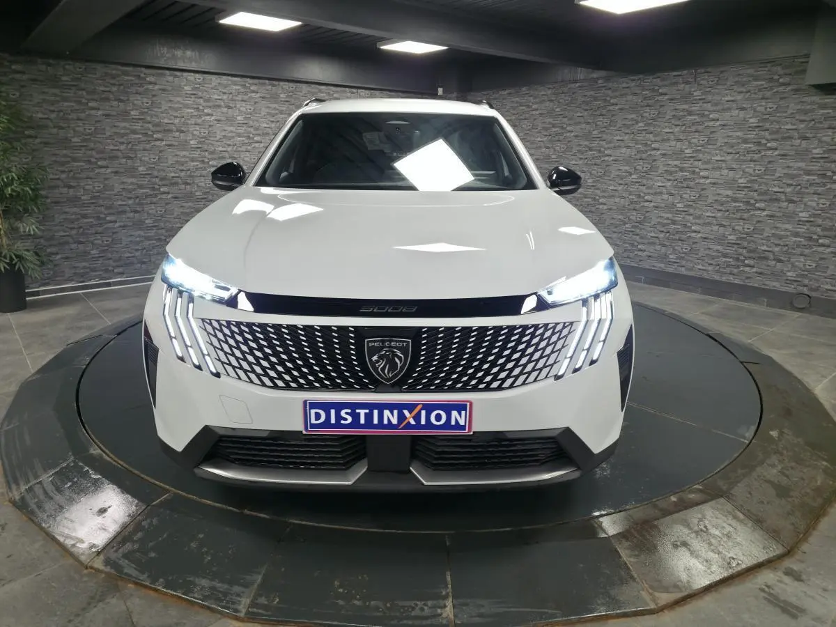 Vue avant d'un Peugeot 5008 blanc 2025 avec calandre noire laquée et feux LED distinctifs allumés.