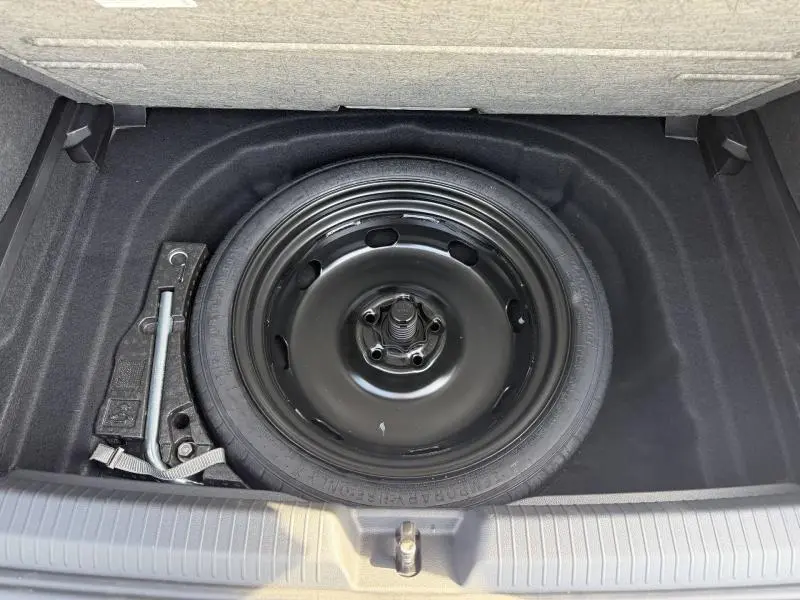 Vue plongeante sur la roue de secours et les outils dans le coffre d'une Volkswagen Golf 2024 Reflet d'Argent métallisée.