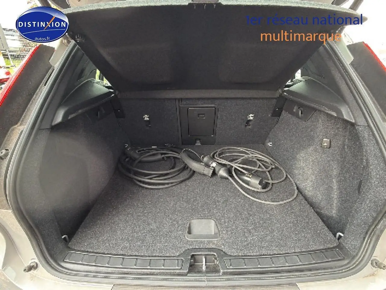 Coffre ouvert vu de l'arrière d'un Volvo XC40 gris 2023 avec câbles de recharge hybride visibles.