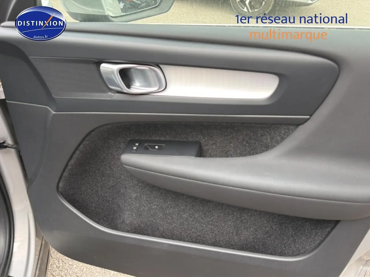 Intérieur côté gauche de la porte avant grise du Volvo XC40 T4 hybride, avec poignée argentée et commande de vitre.