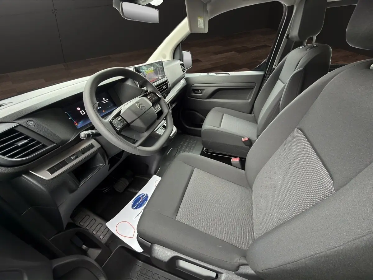Vue intérieure côté conducteur du Citroën Jumpy gris foncé, avec tableau de bord moderne et sièges tissu gris.