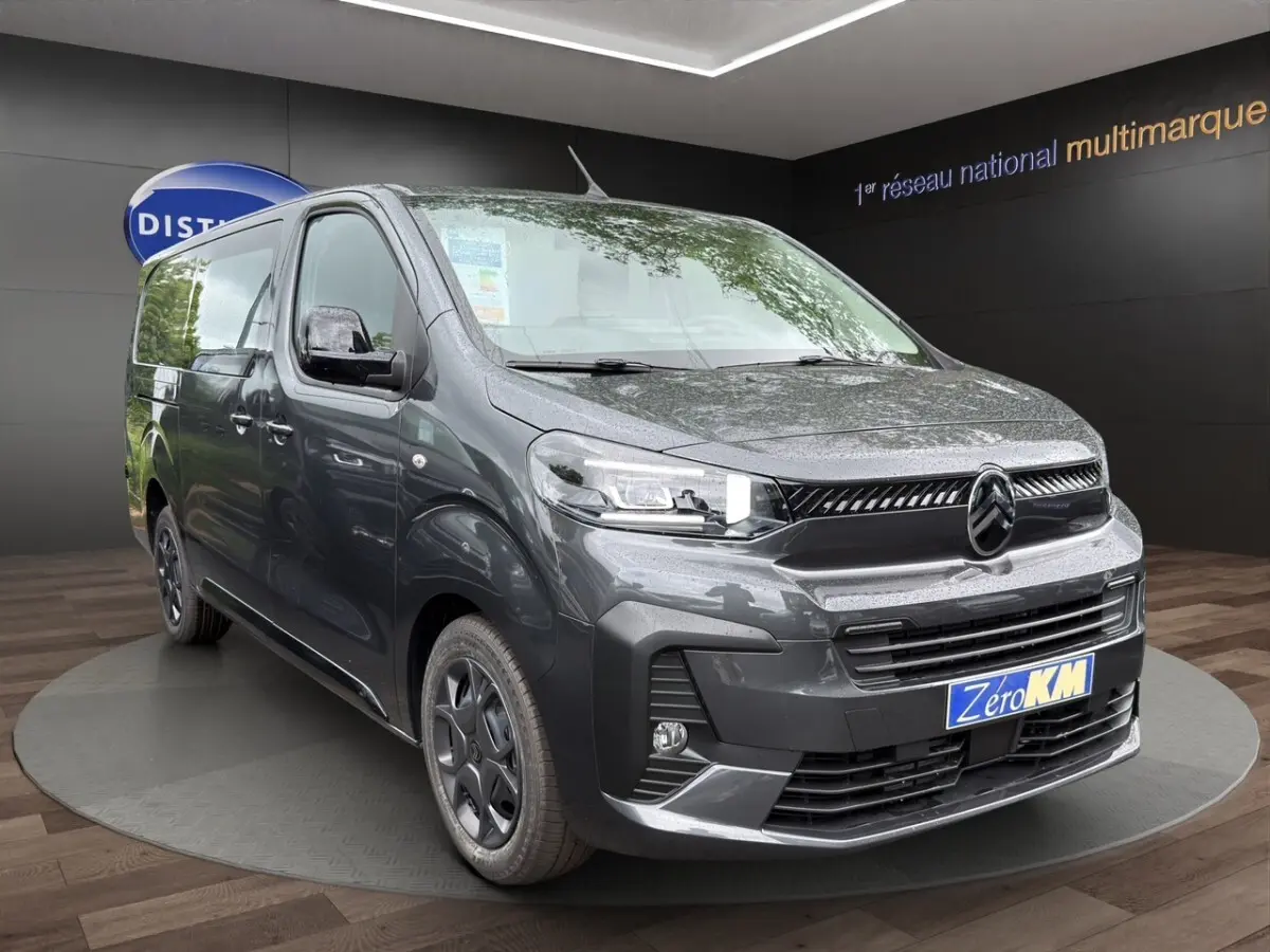 Vue 3/4 avant d'un Citroën Jumpy XL gris foncé avec phares LED et jantes noires en présentation showroom.