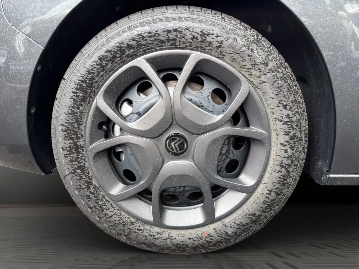 Gros plan sur la roue arrière droite d’un Citroën Jumpy gris foncé avec traces de boue sur le pneu.