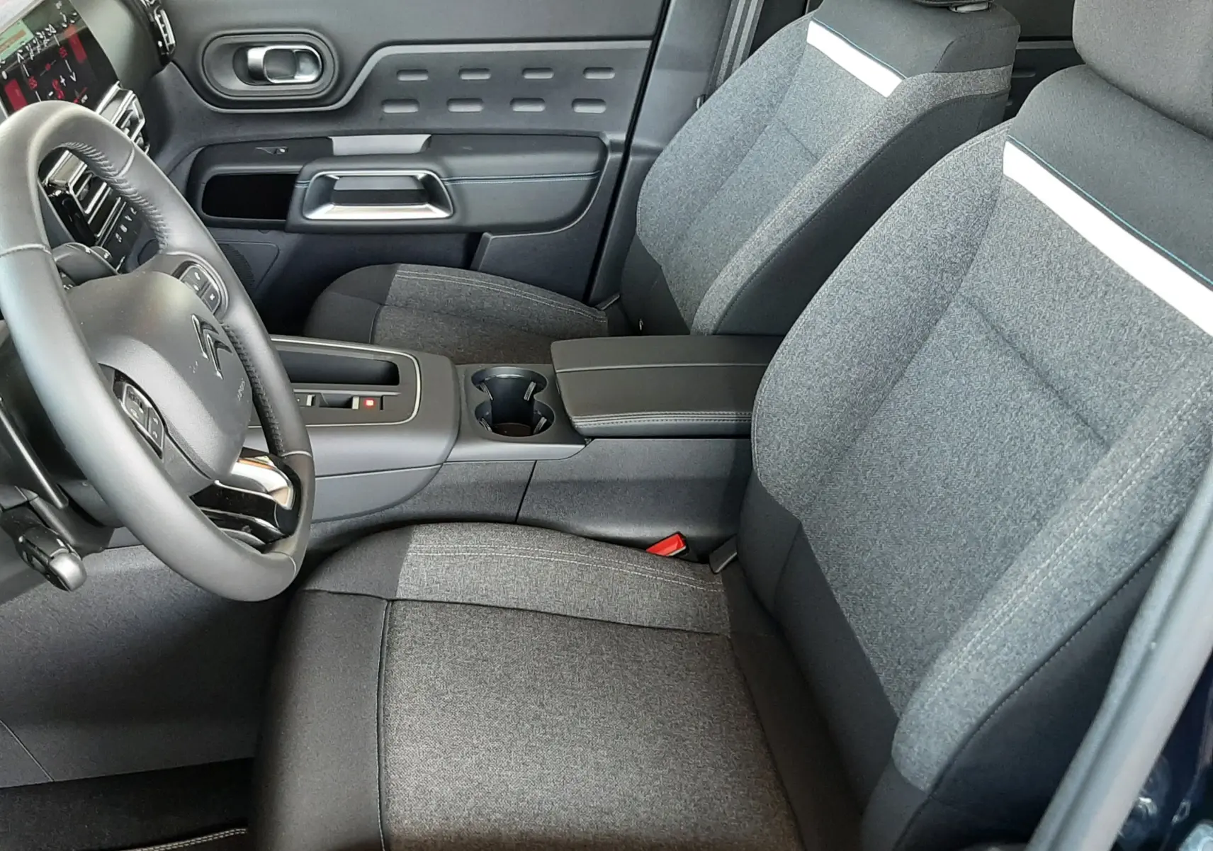 Vue intérieure côté conducteur du Citroën C5 Aircross 2025, sièges tissu gris avec bande blanche et console centrale noire.