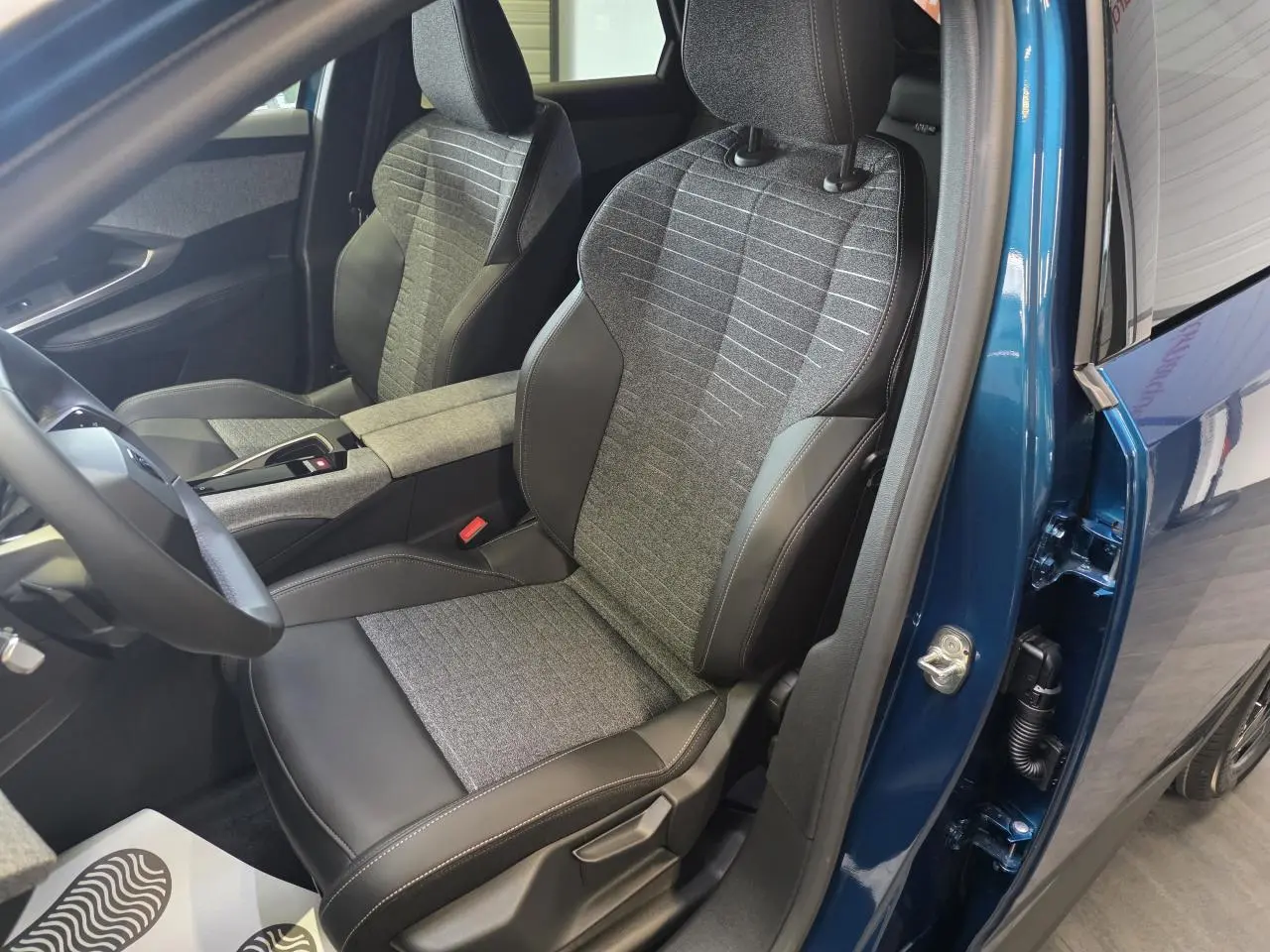 Vue intérieure côté conducteur du Peugeot 3008 bleu 2026, sièges tissu gris et cuir noir avec surpiqûres contrastées.