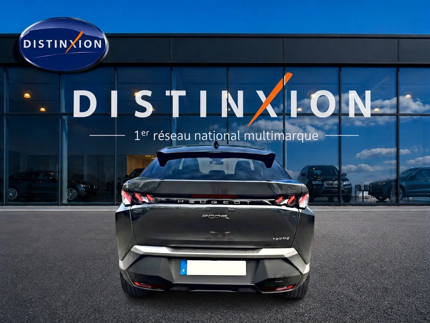 Vue arrière d’un Peugeot 3008 gris titane 2025 avec feux LED et becquet arrière, devant une vitrine Distinxion.