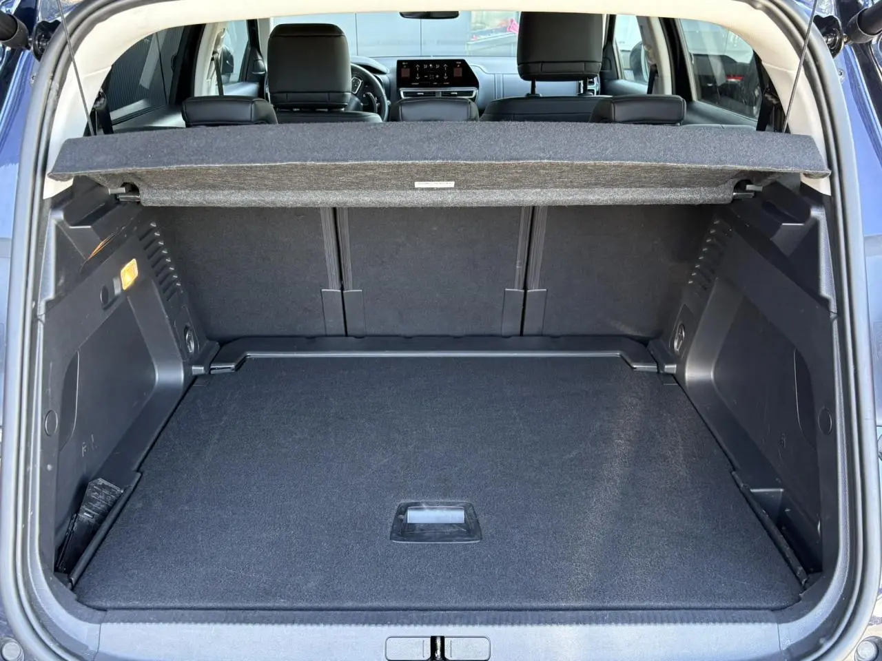 Coffre ouvert vu de l'arrière d'un Citroën C5 Aircross Hybrid bleu Eclipse, avec banquette arrière et tablette cache-bagages visibles.