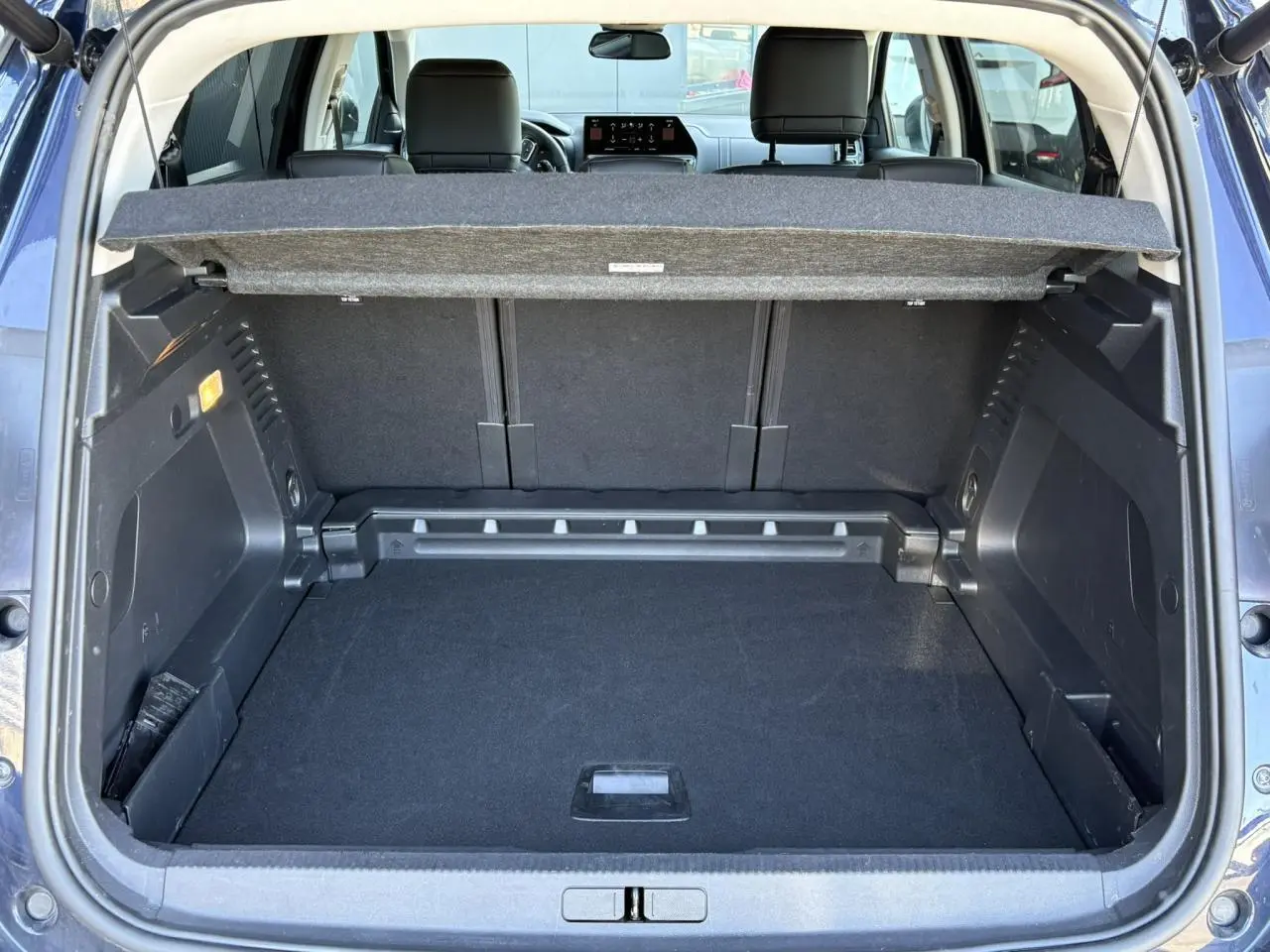 Coffre ouvert vu de l'arrière d'un Citroën C5 Aircross Hybrid bleu Eclipse avec cache-bagages et sièges arrière visibles.