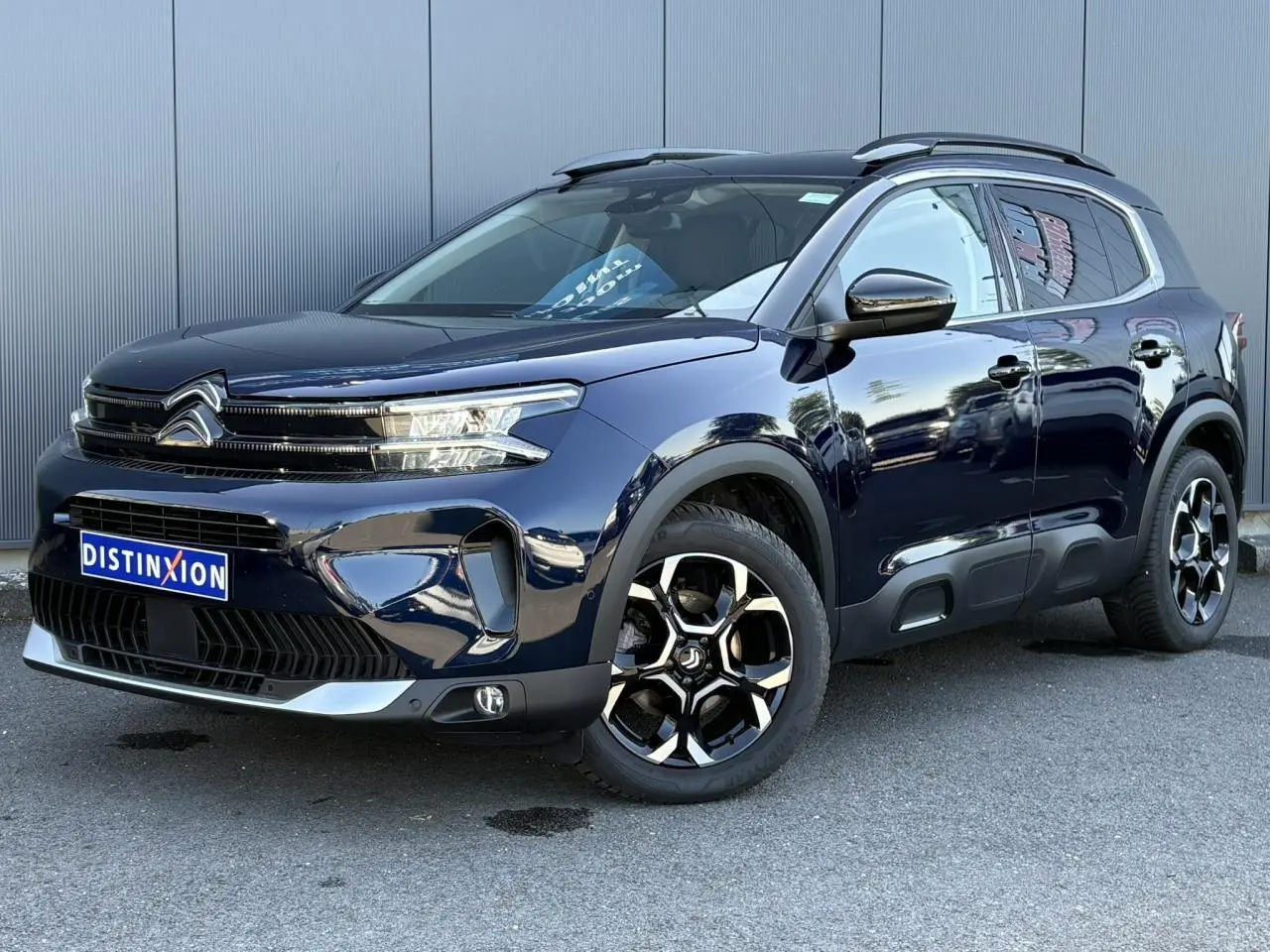 Vue 3/4 avant droite du Citroën C5 Aircross Hybrid 2025 bleu Eclipse avec jantes alliage et barres de toit noires.