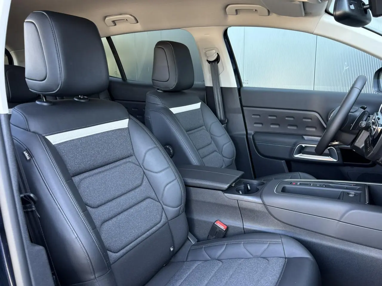 Vue intérieure côté conducteur du Citroën C5 Aircross Hybrid 2025, sièges cuir et tissu gris foncé avec console centrale.