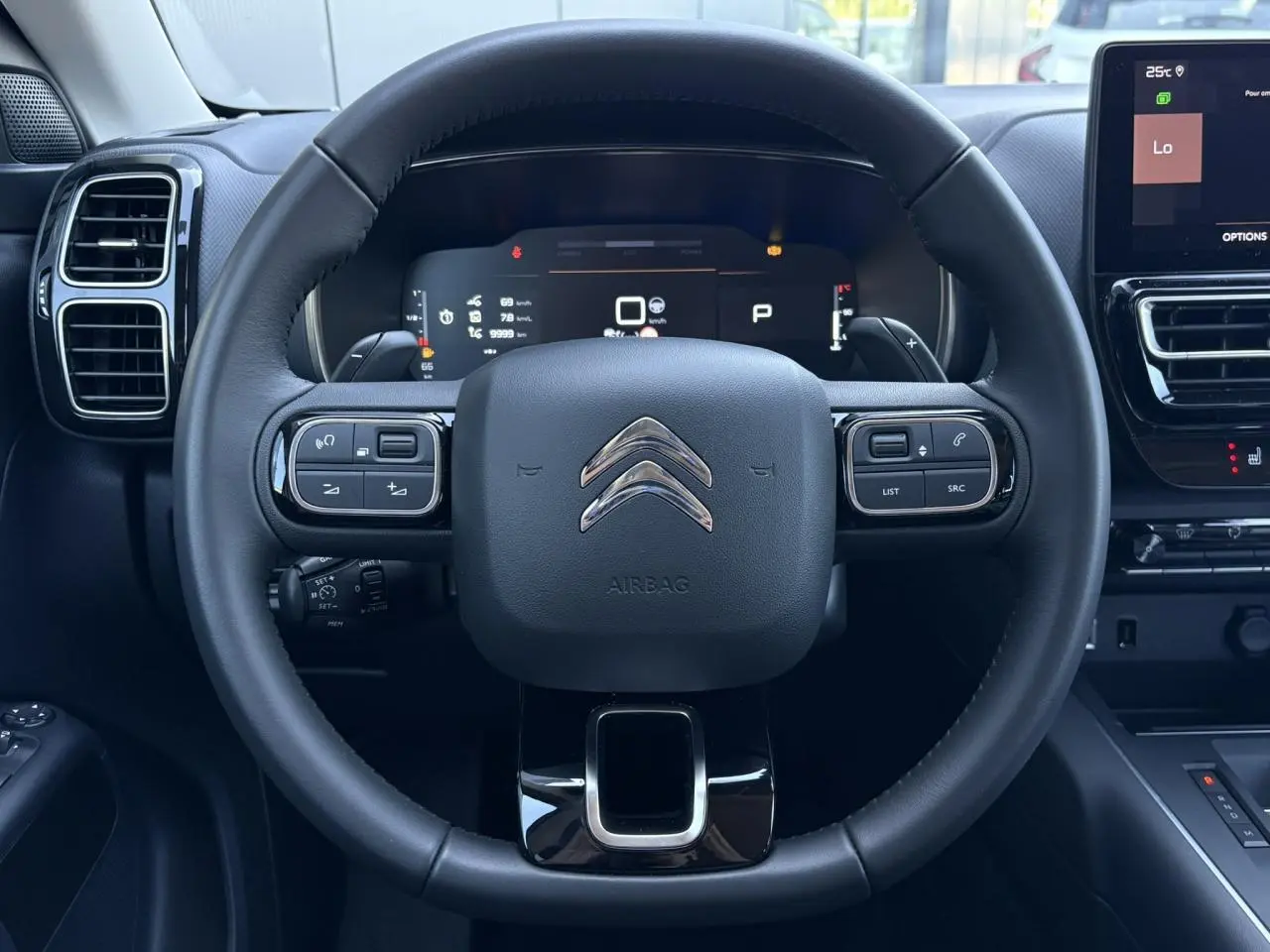 Vue centrée sur le volant noir du Citroën C5 Aircross Hybrid 2025 avec commandes intégrées et tableau de bord numérique.